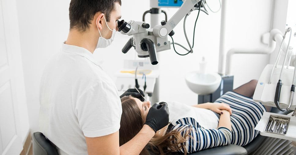 Dentista utilizando microscópio odontológico durante procedimento endodôntico.