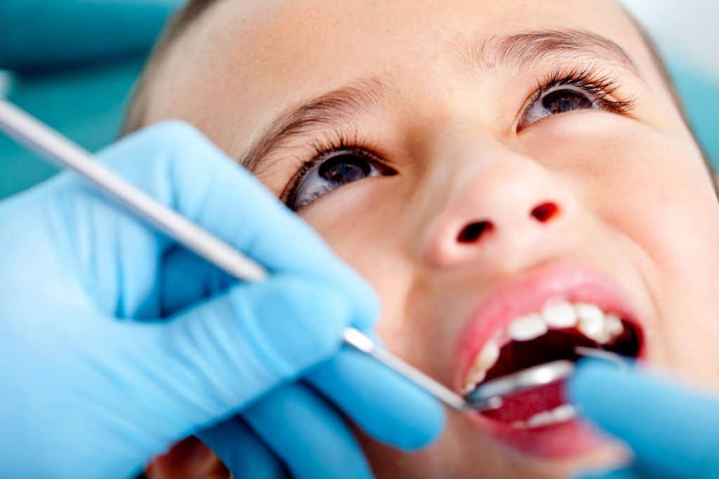 Criança sorrindo em consulta com dentista infantil durante tratamento odontológico