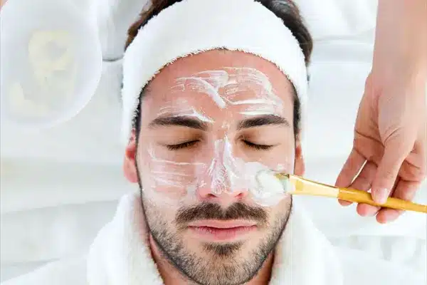 Homem em momento de relaxamento durante limpeza facial estética, em clínica de alto padrão.