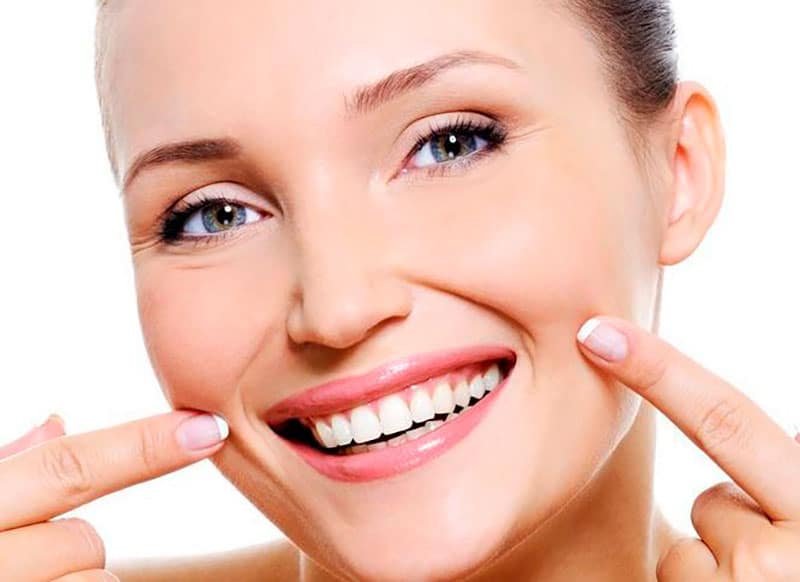 Mulher sorrindo e apontando para as Linhas ao Redor da Boca, ilustrando tratamento estético facial.